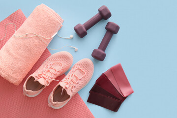 Set of sports equipment with earphones and shoes on color background
