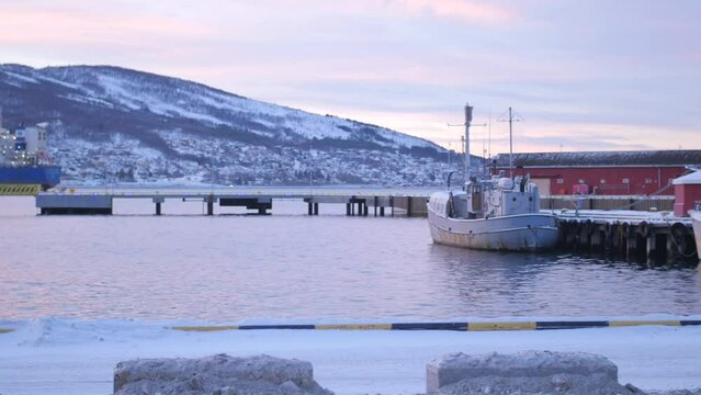 Panning shot across ships and boats moored at dock and pier during polar night above the arctic circle in Narvik, northen Norway with snow covered hills in the background.