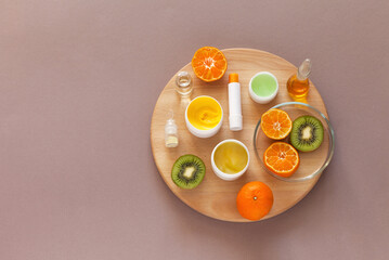 Top view on vitamin and moisturizing natural cosmetics with fruit extract on wooden round podium on beige background. Advertising of new cosmetic products. Anti-aging skin care concept. Copy space