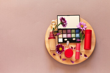 Top view on decorative natural cosmetics with extracts of herbs and flowers on wooden round podium on beige background. Advertising of new cosmetic products. Anti-aging skin care. Copy space, flat lay