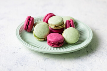 Pink and green macaroons on green plate on white background. Traditional French sweet dessert.