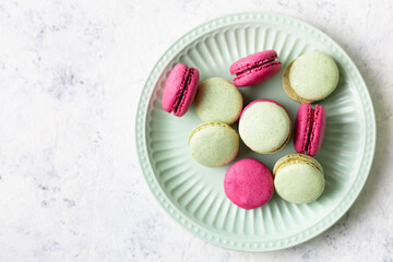 Pink and green macaroons on green plate on white background. Traditional French sweet dessert.