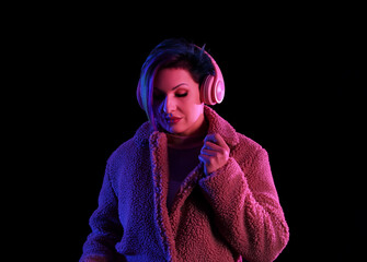 Beautiful woman with unusual hair listening to music on black background