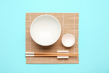 Bamboo mat with Chinese bowls and chopsticks on color background