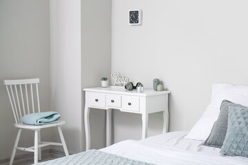 Table with wireless portable speaker and headphones near light wall in bedroom