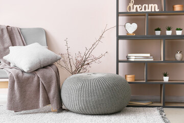 Interior of modern room with pouf, shelf unit and armchair
