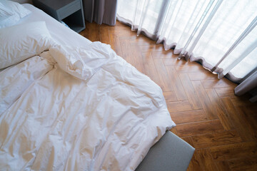 topview white wrinkle blanket mattress pillow in unmade bed with morning sunlight through big window curtain and sheer hotel room waiting for maid to make a bed after use for sleeping,home interior