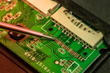 PCB board of a CF, micro SD and SD card reader. Electronic circuit elements and connections on the PCB board. Tapping the circuit board with the screwdriver.