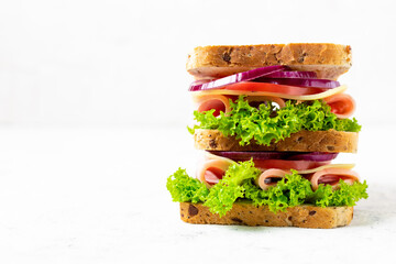 sandwich with ham cheese tomatoes lettuce onions. Multi-layer sandwich with whole grain bread on white background.