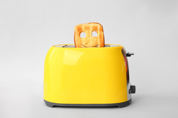 Funny slice of bread in toaster on light background