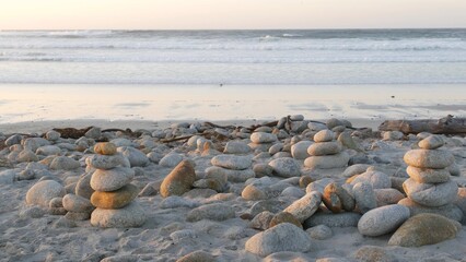 Rock balancing on pebble beach, Monterey 17-mile drive, California coast, USA. Stable pyramid stacks of round stones, sea ocean water waves crashing at sunset. Serenity harmony, calm zen meditation.