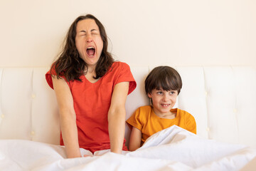 Obraz na płótnie Canvas A child with mom sit on the bed, woman yawns, morning awakening
