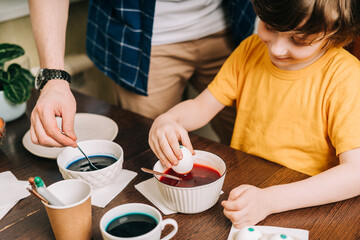 Obraz na płótnie Canvas Easter day. Male Father and son painting eggs on wooden background. Family sitting in a kitchen. Preparing for Easter, creative homemade decoration. Child kid boy having fun and painting easter eggs