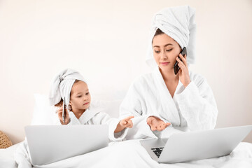 Little daughter with her working mother in bedroom