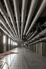 Ceiling mounted industrial pipelines inside underground  building, Long corridor with metal floors,...