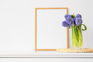 Blank photo frame and vase with hyacinth flowers on shelf near white wall