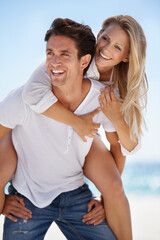 Fun in the sun. A handsome young boyfriend giving his girlfriend a piggyback ride on the beach.