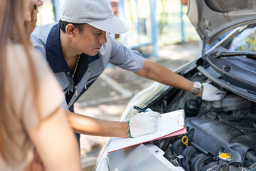 Fototapeta na wymiar Asian male auto mechanic holds a clipboard and examines car engine breakdown problem with women customer and explain the root cause and estimate repair quotation, Car repair, and maintenance concept.