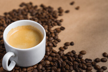 Small white coffee cup with espresso crema on roasted beans at brown background. Mock up