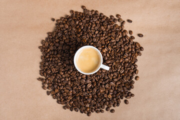 Small white coffee cup with espresso crema on roasted beans at brown background. Mock up