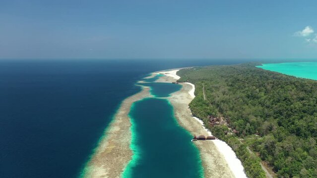 Drone view of lagoon formation when is low tide on a tropical island with a dock seen by far, open blue water on one side and turquoise waters on the other side