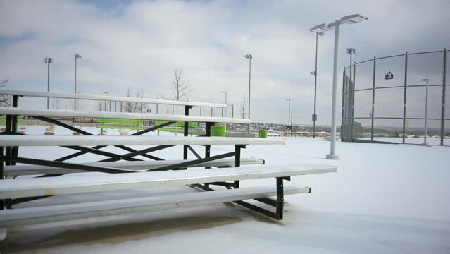 Bleachers at baseball and softball fields covered in fresh snow during the winter, pan handheld