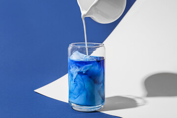 Pouring milk in glass with blue matcha tea on color background