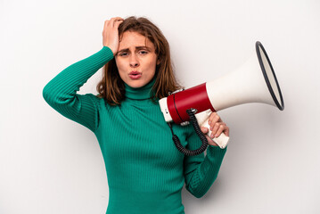 Young caucasian woman holding a megaphone isolated on white background being shocked, she has remembered important meeting.