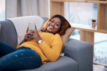 Obraz premium Home is my happy place. Shot of an attractive young woman using her cellphone while relaxing on the sofa at home.
