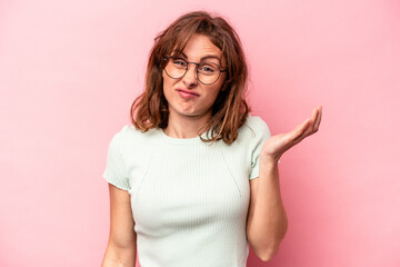 Young caucasian woman isolated on pink background doubting and shrugging shoulders in questioning...