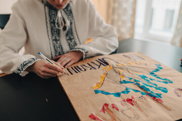 Obraz premium child in national ethnic embroidered white shirt draws poster in support of Ukraine, writes slogan against Russia's military actions