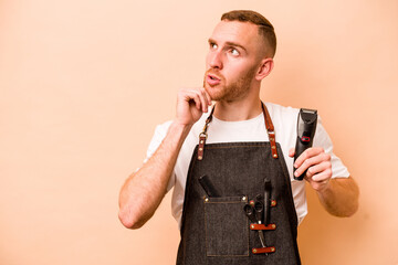 Young hairdresser caucasian man isolated on beige background looking sideways with doubtful and...