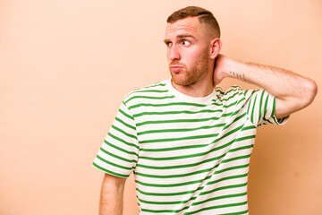 Young caucasian man isolated on beige background touching back of head, thinking and making a...