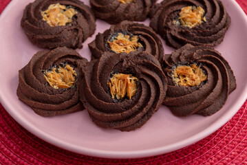 Chocolate cookies with brown cream on pink round plate. Image from above