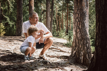 Father and little son holding hands walking in summer pine forest together. Hyper-local travel,...