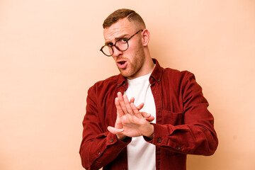 Young caucasian man isolated on beige background doing a denial gesture
