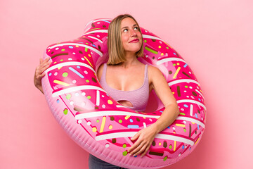 Obraz na płótnie Canvas Young caucasian woman holding an air mattress isolated on pink background dreaming of achieving goals and purposes