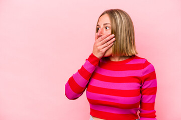 Young caucasian woman isolated on pink background thoughtful looking to a copy space covering mouth with hand.