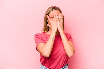 Young caucasian woman isolated on pink background blink at the camera through fingers, embarrassed covering face.