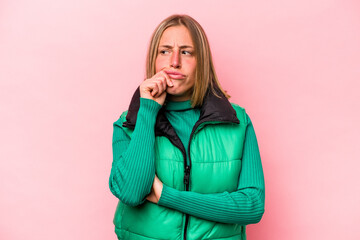 Young caucasian woman isolated on pink background thinking and looking up, being reflective, contemplating, having a fantasy.