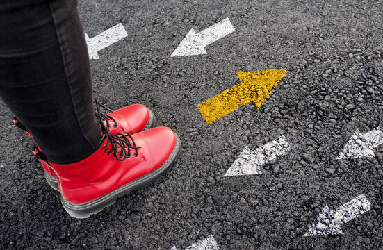 Woman Boots On Asphalt And Opposing Direction Arrows On Asphalt Ground, Personal Perspective Footsie Concept For Finding Your Own Way
