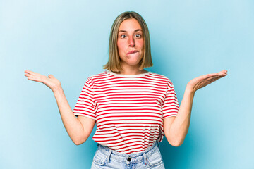 Young caucasian woman isolated on blue background confused and doubtful shrugging shoulders to hold a copy space.