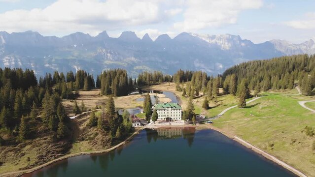 Aerial flyover over Seebenalp at Flumserberg, Switzerland from the alpine lake and historical hotel towards lake Walensee and the surrounding cliffs and sharp mountain peaks of Churfirsten
