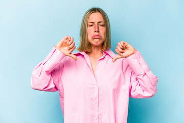 Young caucasian woman isolated on blue background showing a dislike gesture, thumbs down....