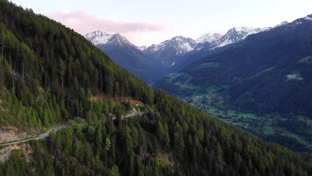 Aerial flyover over a forest road in Val d' Anniviers near St. Luc, Switzerland with a view of the peaks around Zinal and Grimentz at the end of a summer day