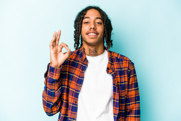 Young African American man isolated on blue background cheerful and confident showing ok gesture.