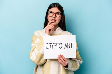 Fototapeta na wymiar Young caucasian business woman holding a crypto art placard isolated on blue background relaxed thinking about something looking at a copy space.