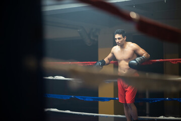 Sweaty shirtless boxer leaning on rope of ring. Through ropes view of brunette Portuguese sportsman...
