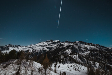 Vertical photo of snow-capped mountains at night with stars and a meteor in the sky