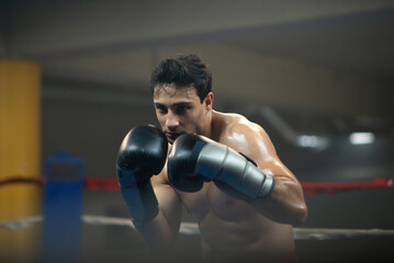Young boxer attacking competitio in ring during competition. Focused shirtless man in boxing gloves...